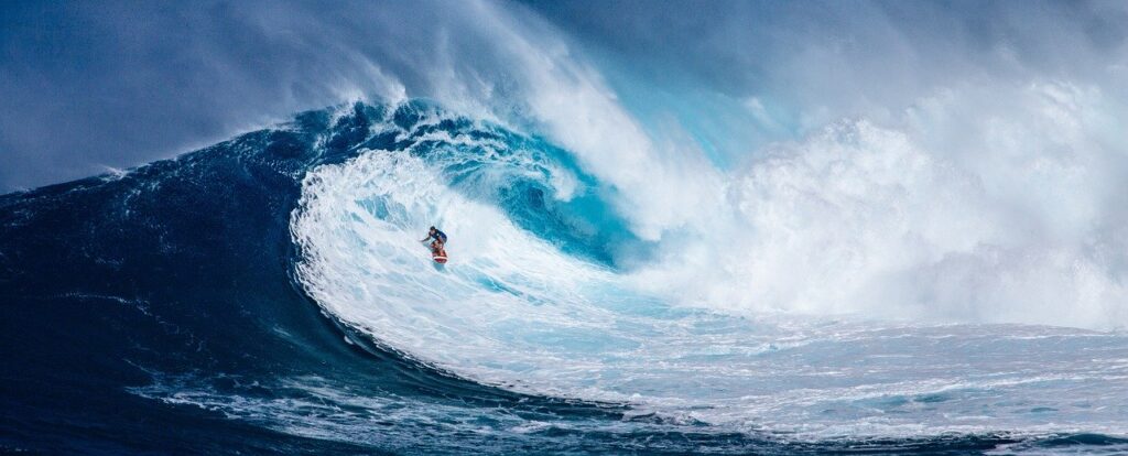 a usrfer crouched down riding horizontal across a wave emerging from inside of the top of the wave curl (getting barreled). Good analogy for your Covid-19 playbook to successfully emerge from inside the wave